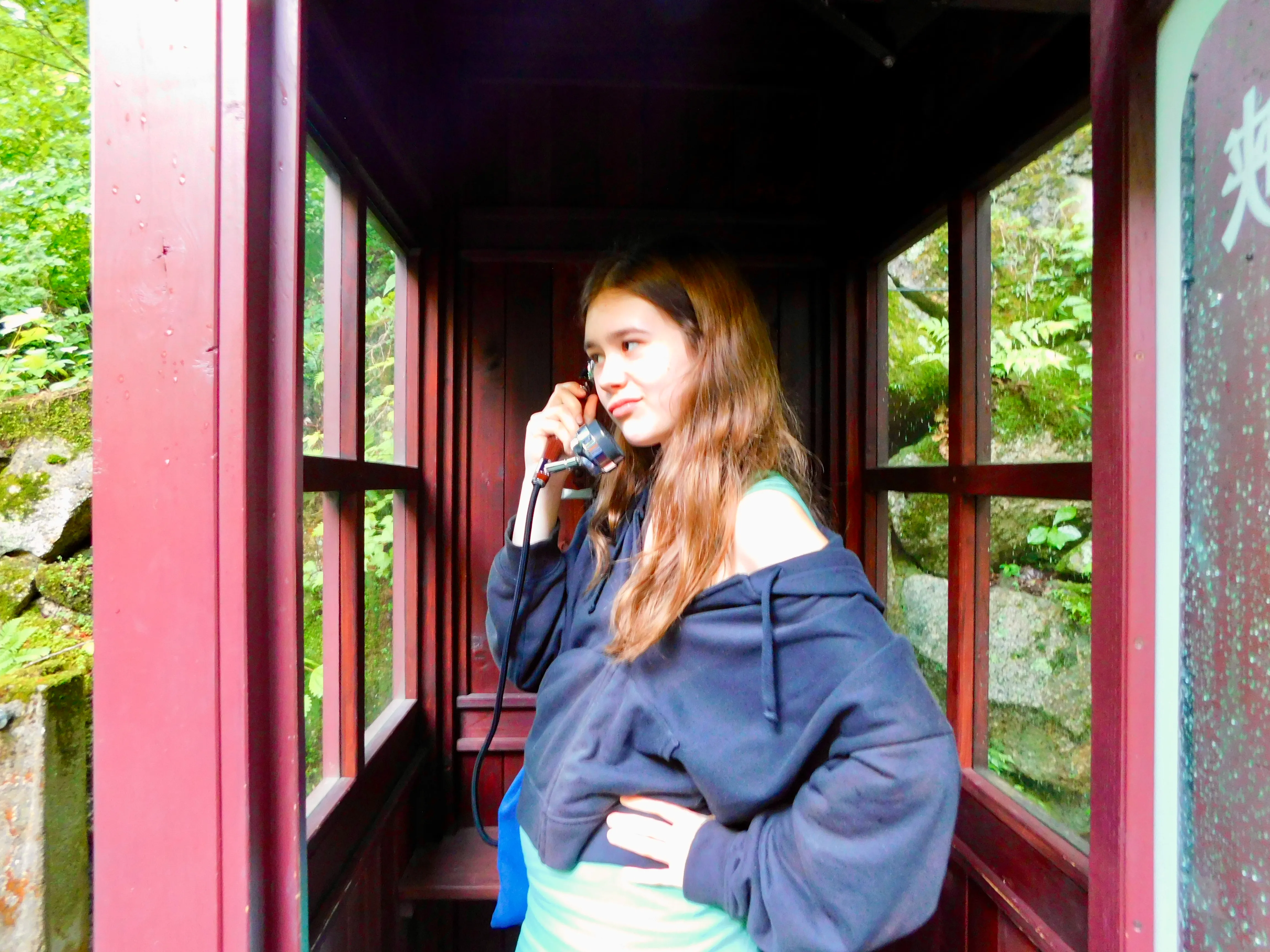 Lalie Lours (Best Teen Book Review Site) photo in a phone booth wearing green dress and black sweater answering the phone.